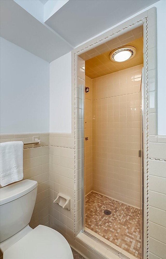 full bathroom with a shower stall, toilet, wainscoting, and tile walls