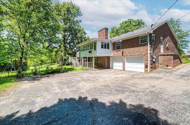 back of property with brick siding, a chimney, an attached garage, asphalt driveway, and stairway