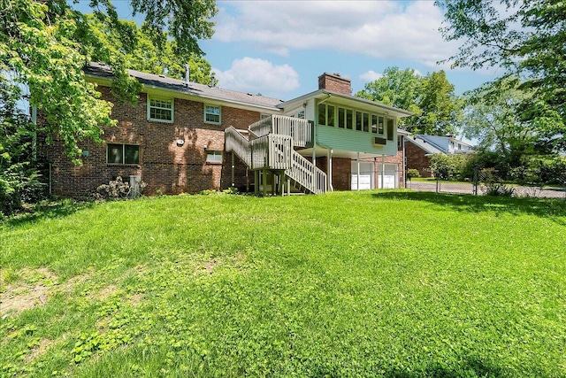 back of house featuring a chimney, stairway, a garage, brick siding, and a yard