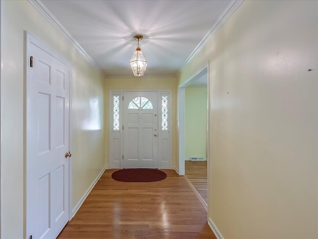entryway with wood finished floors, crown molding, and baseboards