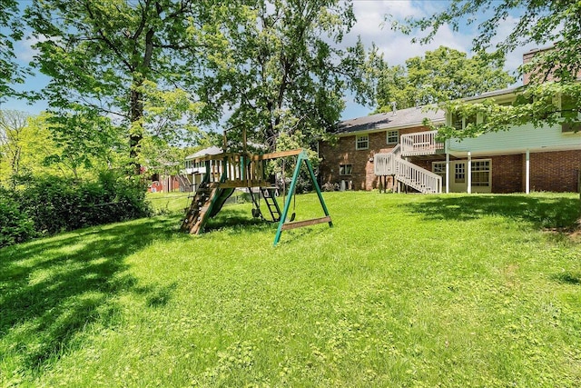 view of green lawn featuring a playground, stairs, and a wooden deck