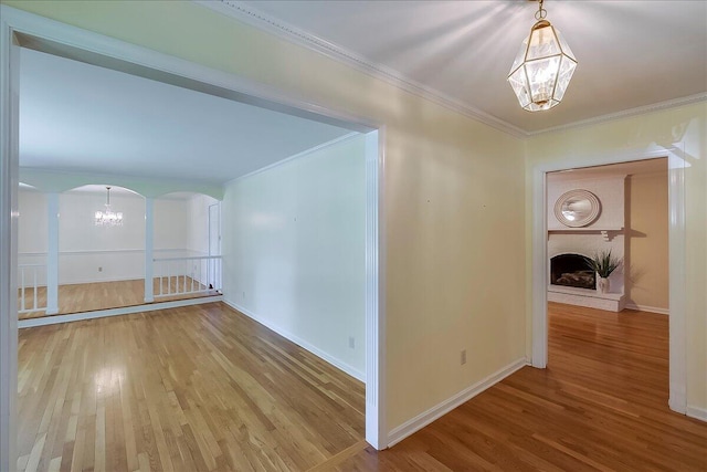 corridor with a chandelier, wood finished floors, arched walkways, ornamental molding, and baseboards