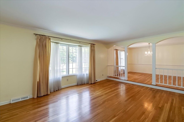 empty room featuring arched walkways, a chandelier, crown molding, wood finished floors, and baseboards