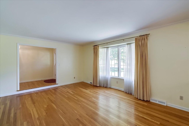 empty room with ornamental molding, light wood-type flooring, and baseboards