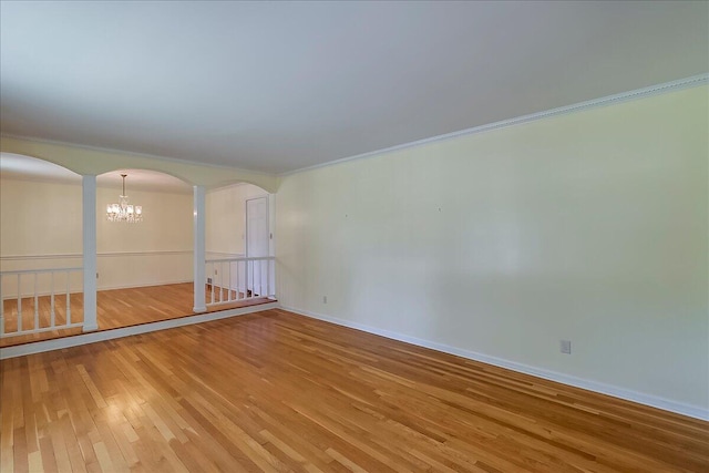 spare room with arched walkways, light wood-type flooring, a chandelier, ornamental molding, and baseboards