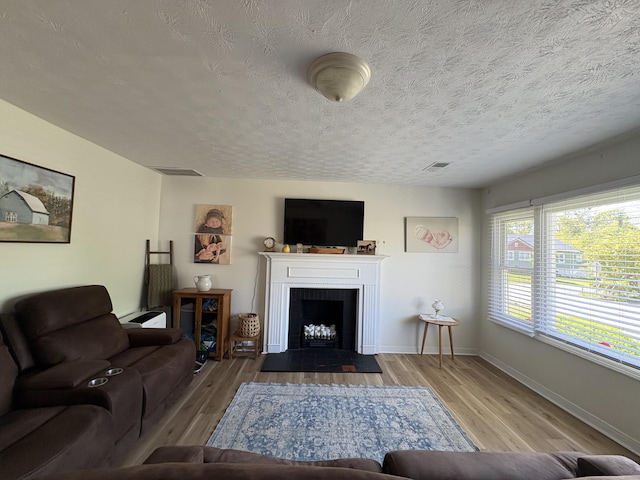 living room with wood finished floors, baseboards, a textured ceiling, and a fireplace with flush hearth