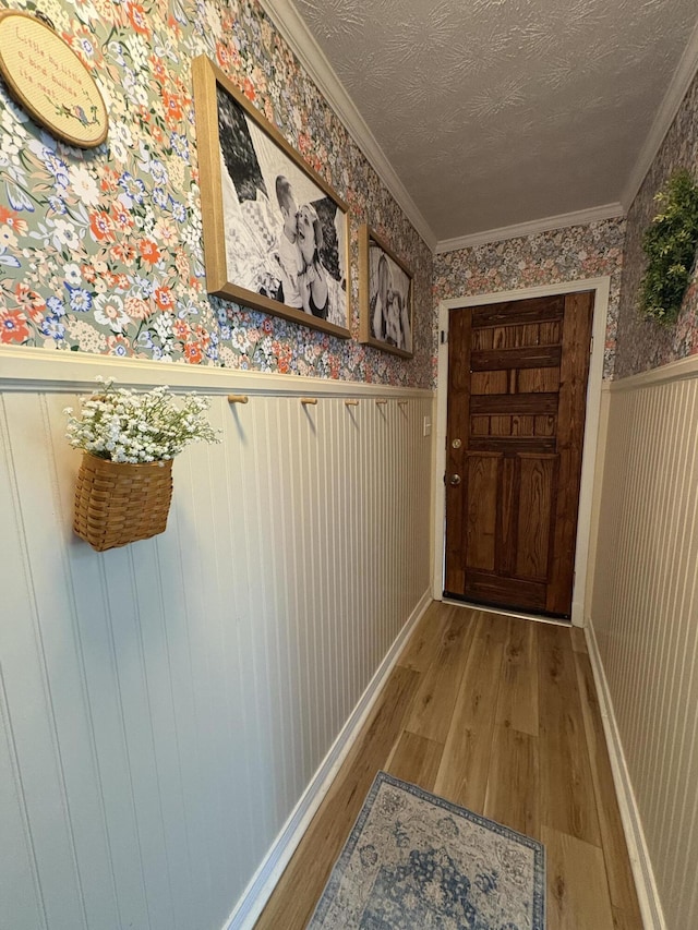 entryway with wallpapered walls, a wainscoted wall, wood finished floors, ornamental molding, and a textured ceiling