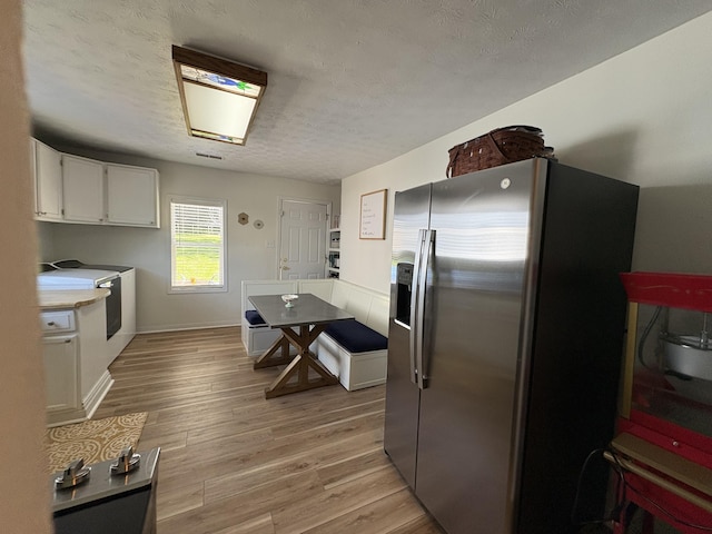 kitchen with stainless steel fridge, white cabinetry, light wood-type flooring, a textured ceiling, and light countertops