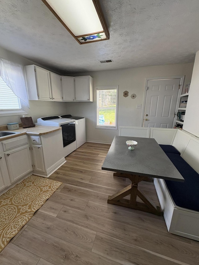 kitchen with white cabinets, independent washer and dryer, wood finished floors, light countertops, and a textured ceiling