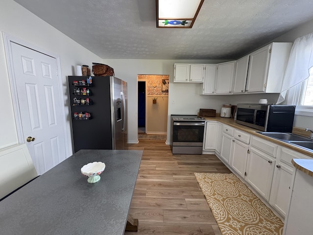 kitchen featuring stainless steel appliances, a sink, light wood-style flooring, white cabinets, and a textured ceiling