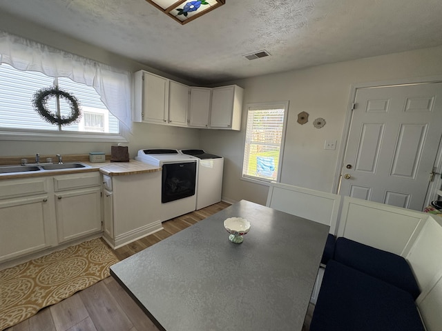 kitchen featuring independent washer and dryer, a sink, light wood-style flooring, healthy amount of natural light, and a textured ceiling