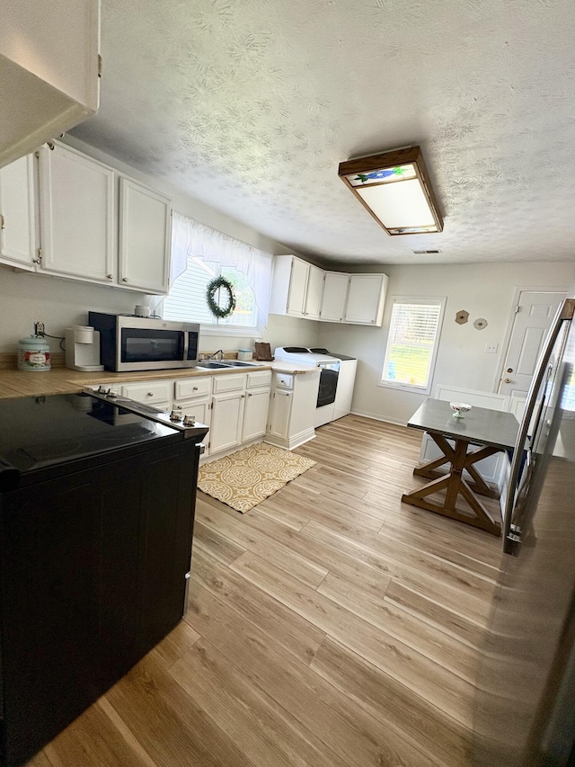 kitchen featuring stainless steel microwave, a textured ceiling, light wood-type flooring, white cabinets, and a sink
