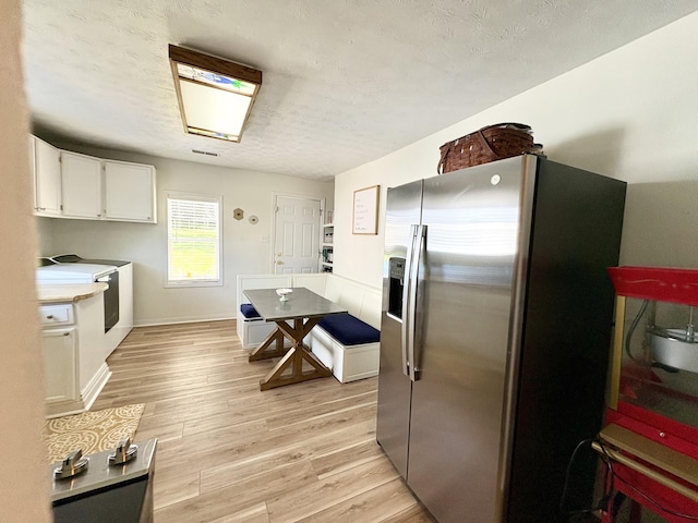 kitchen featuring stainless steel fridge with ice dispenser, white cabinets, light wood-style flooring, a textured ceiling, and light countertops