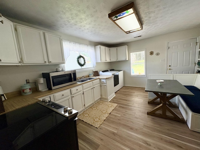 kitchen with stainless steel microwave, a textured ceiling, white cabinetry, light wood-type flooring, and light countertops