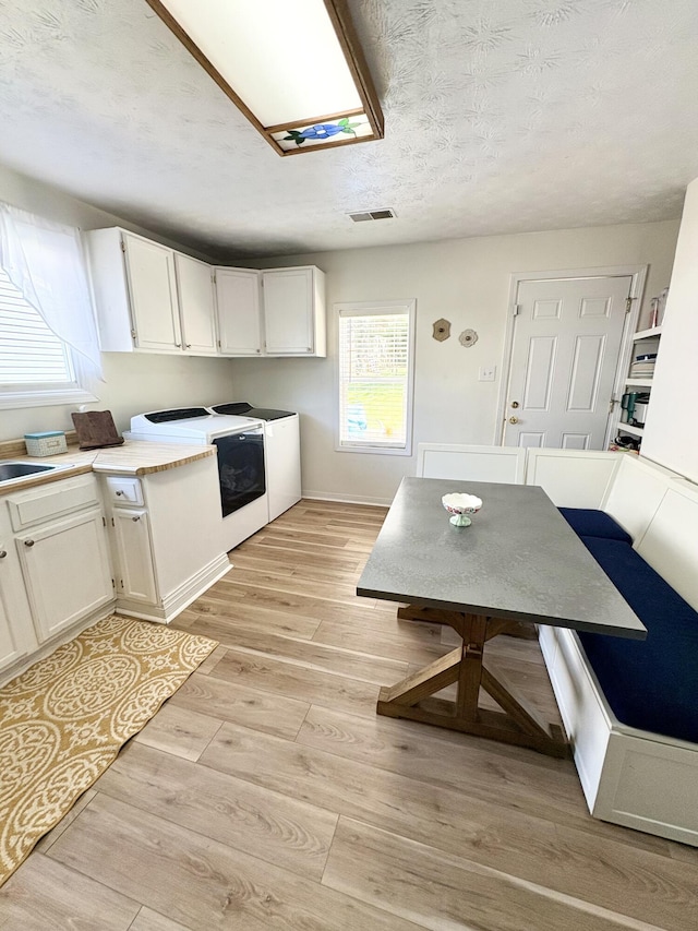kitchen featuring washing machine and clothes dryer, light wood-type flooring, white cabinets, light countertops, and a textured ceiling