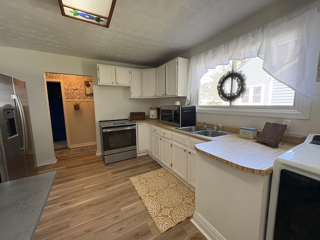 kitchen featuring stainless steel appliances, washer / dryer, a sink, white cabinets, and a textured ceiling