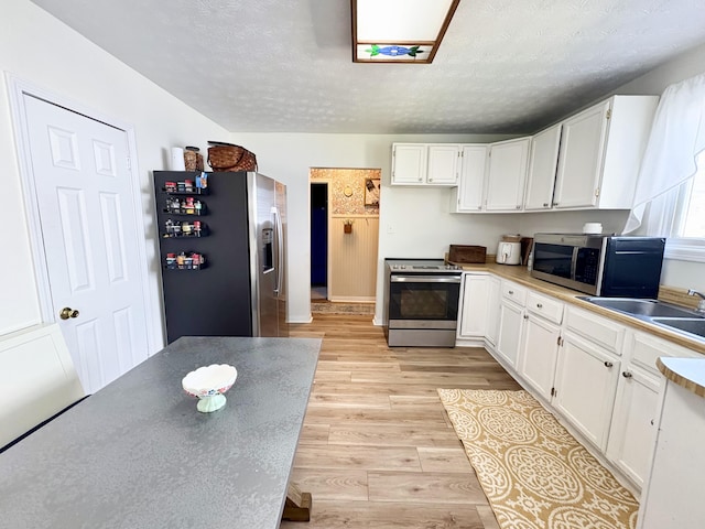 kitchen featuring appliances with stainless steel finishes, a sink, light wood-style floors, a textured ceiling, and white cabinetry