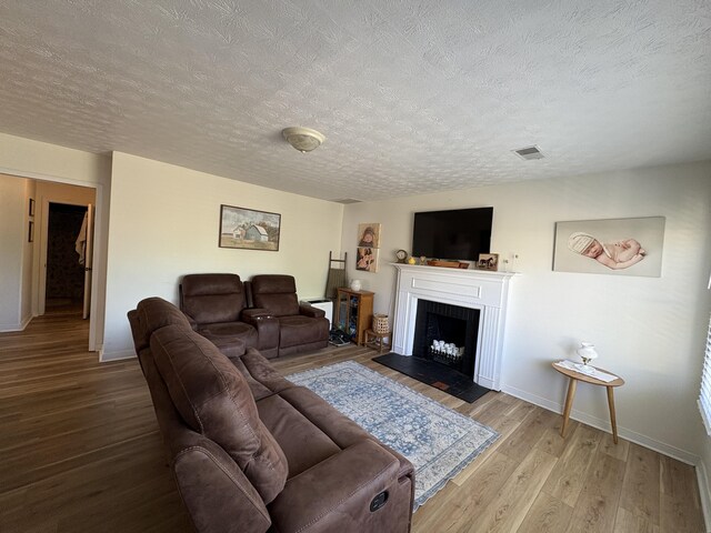 living area with a textured ceiling, wood finished floors, a fireplace with raised hearth, and baseboards