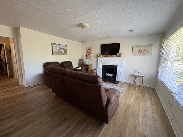 living room with a textured ceiling, wood finished floors, a fireplace with flush hearth, and baseboards