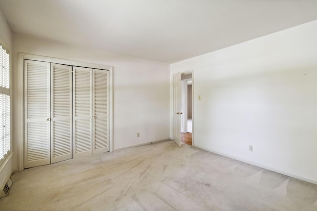 unfurnished bedroom featuring light colored carpet, a closet, and baseboards