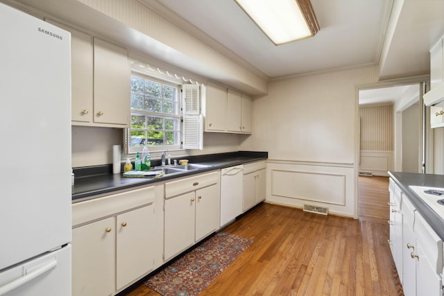 kitchen with white appliances, a sink, ornamental molding, dark countertops, and light wood finished floors