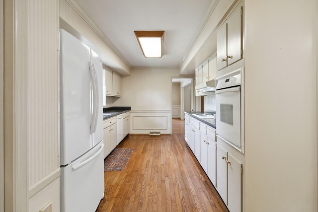 kitchen with white appliances, under cabinet range hood, crown molding, dark countertops, and light wood-style flooring