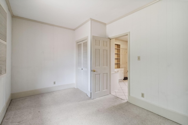 unfurnished bedroom with a closet, crown molding, carpet flooring, and baseboards