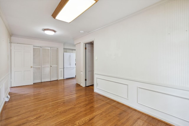 unfurnished bedroom with freestanding refrigerator, ornamental molding, a closet, a decorative wall, and light wood finished floors