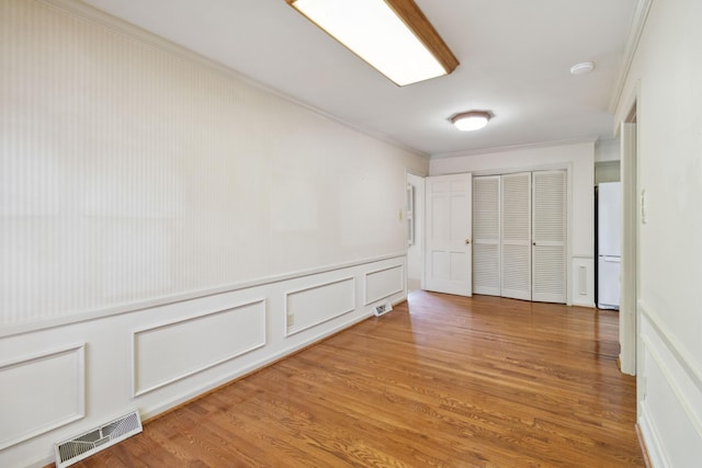 unfurnished bedroom with crown molding, a closet, wood finished floors, a decorative wall, and freestanding refrigerator
