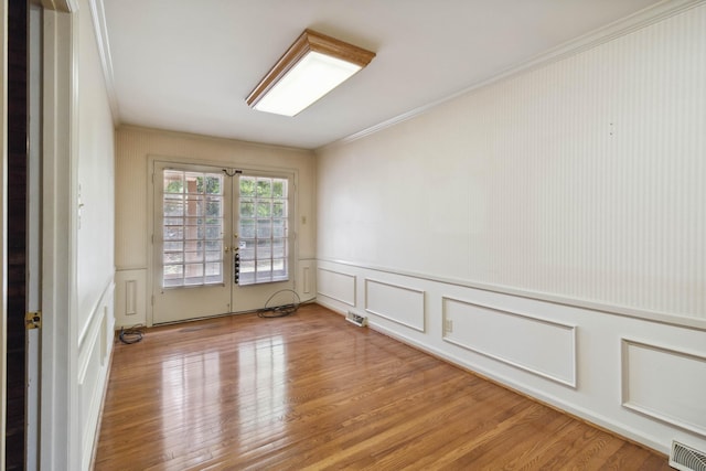 unfurnished room featuring a decorative wall, french doors, ornamental molding, light wood-type flooring, and a wainscoted wall