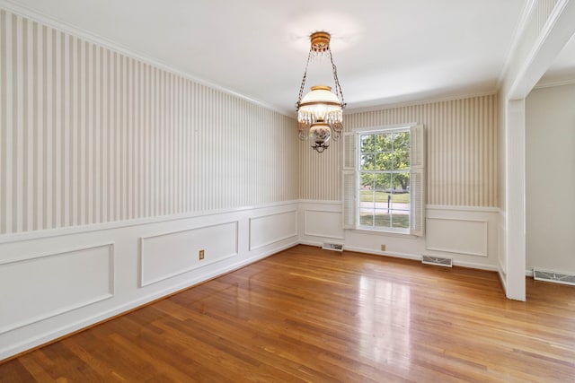 unfurnished room with a chandelier, ornamental molding, wallpapered walls, light wood finished floors, and a decorative wall