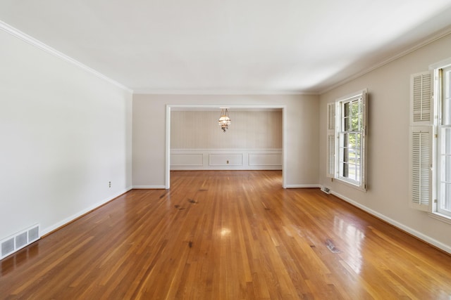 empty room featuring a chandelier, wood finished floors, crown molding, and baseboards