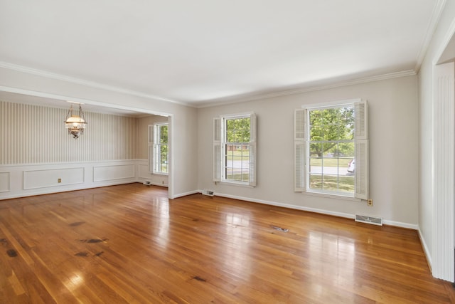 empty room with wood finished floors, ornamental molding, baseboards, and a chandelier