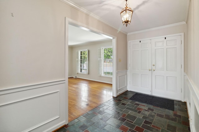 foyer entrance with a chandelier, crown molding, dark stone finish floors, and a wainscoted wall