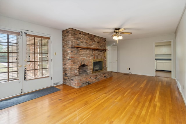 unfurnished living room with ceiling fan, wood finished floors, a brick fireplace, and baseboards