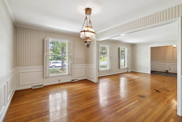 spare room with a decorative wall, ornamental molding, a chandelier, a wainscoted wall, and wood finished floors