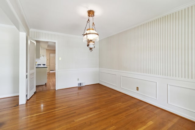 unfurnished dining area featuring ornamental molding, a chandelier, a wainscoted wall, wood finished floors, and baseboards