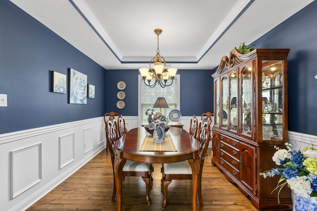 dining area with a chandelier, a raised ceiling, wood finished floors, a wainscoted wall, and ornamental molding