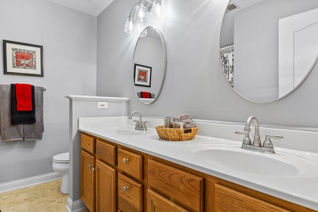 full bathroom featuring toilet, baseboards, and double vanity