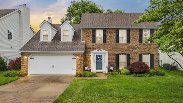 colonial home with a front yard, an attached garage, concrete driveway, roof with shingles, and brick siding
