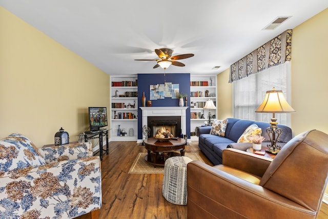 living room featuring ceiling fan, wood finished floors, a lit fireplace, and built in features