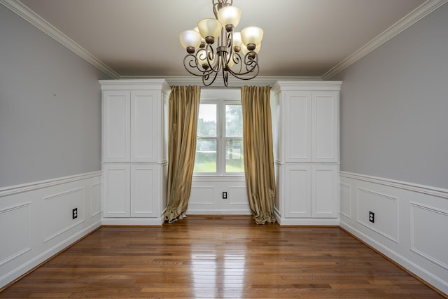 unfurnished dining area featuring a chandelier, crown molding, wood finished floors, a decorative wall, and wainscoting