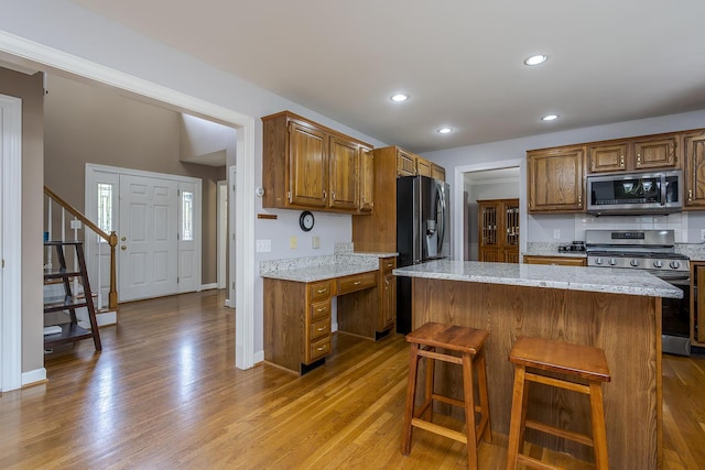 kitchen featuring stainless steel appliances, wood finished floors, light stone counters, and recessed lighting