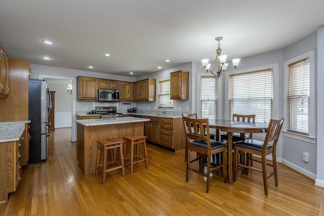 kitchen featuring stainless steel appliances, a chandelier, light wood finished floors, a center island, and brown cabinetry