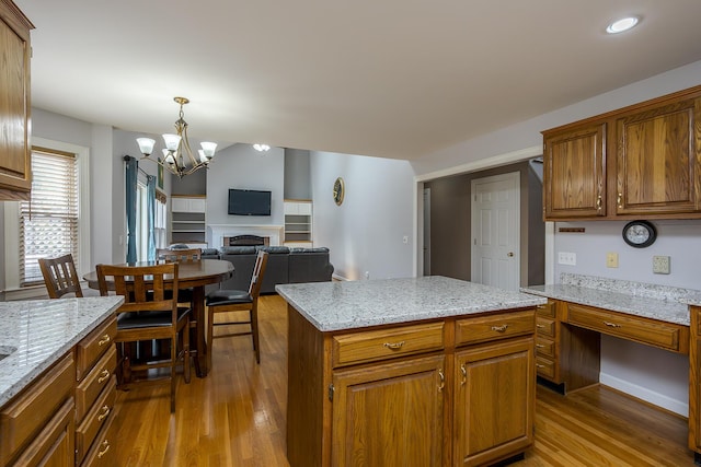 kitchen featuring wood finished floors, a chandelier, a fireplace, brown cabinetry, and a center island