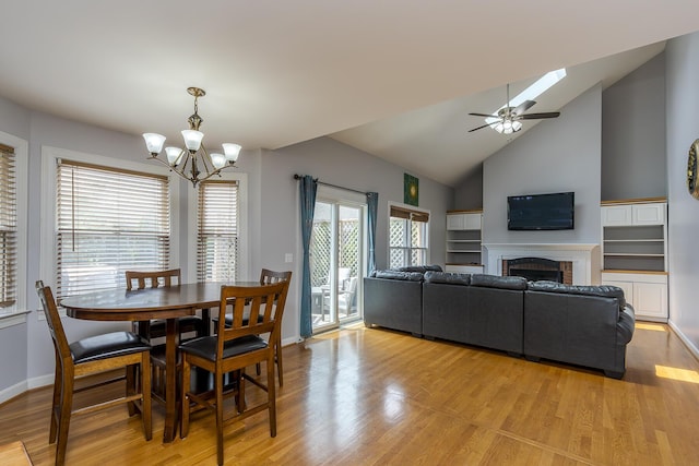 dining area featuring light wood-type flooring, a chandelier, a brick fireplace, and high vaulted ceiling