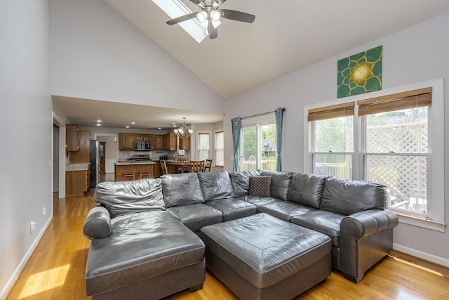 living room with high vaulted ceiling, baseboards, a chandelier, ceiling fan, and light wood-style floors