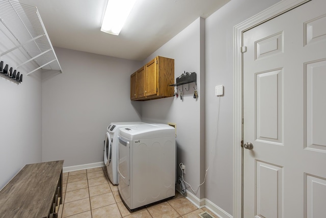clothes washing area with washing machine and dryer, cabinet space, light tile patterned floors, and baseboards