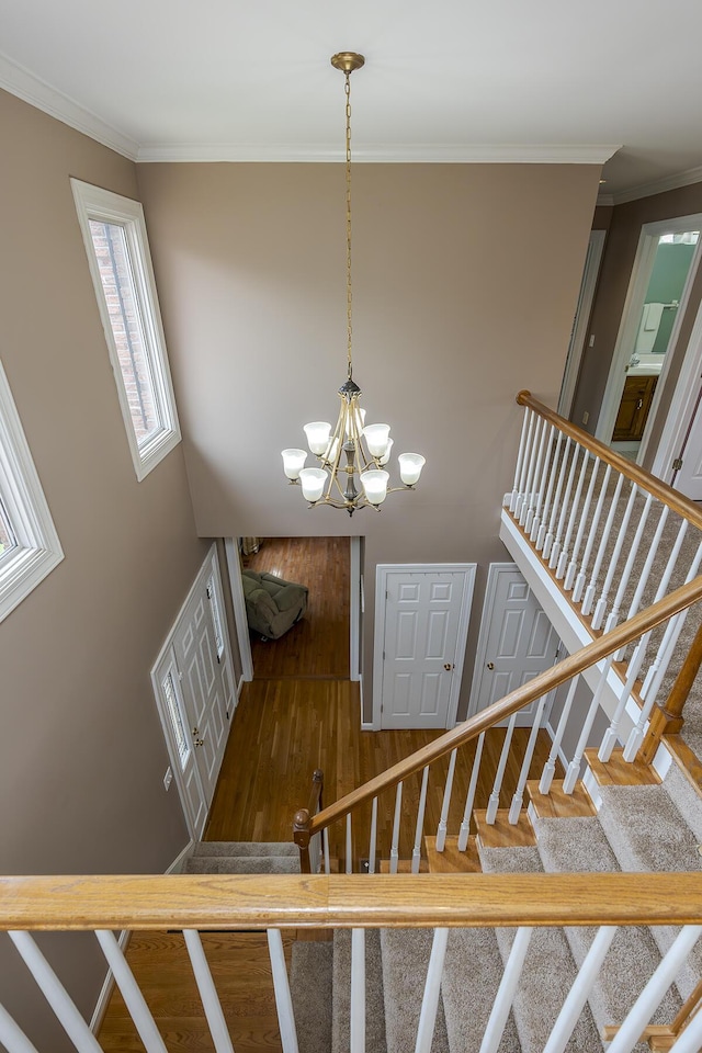 stairway featuring wood finished floors, ornamental molding, and a chandelier