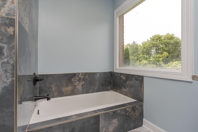 bathroom with healthy amount of natural light, a bath, and baseboards
